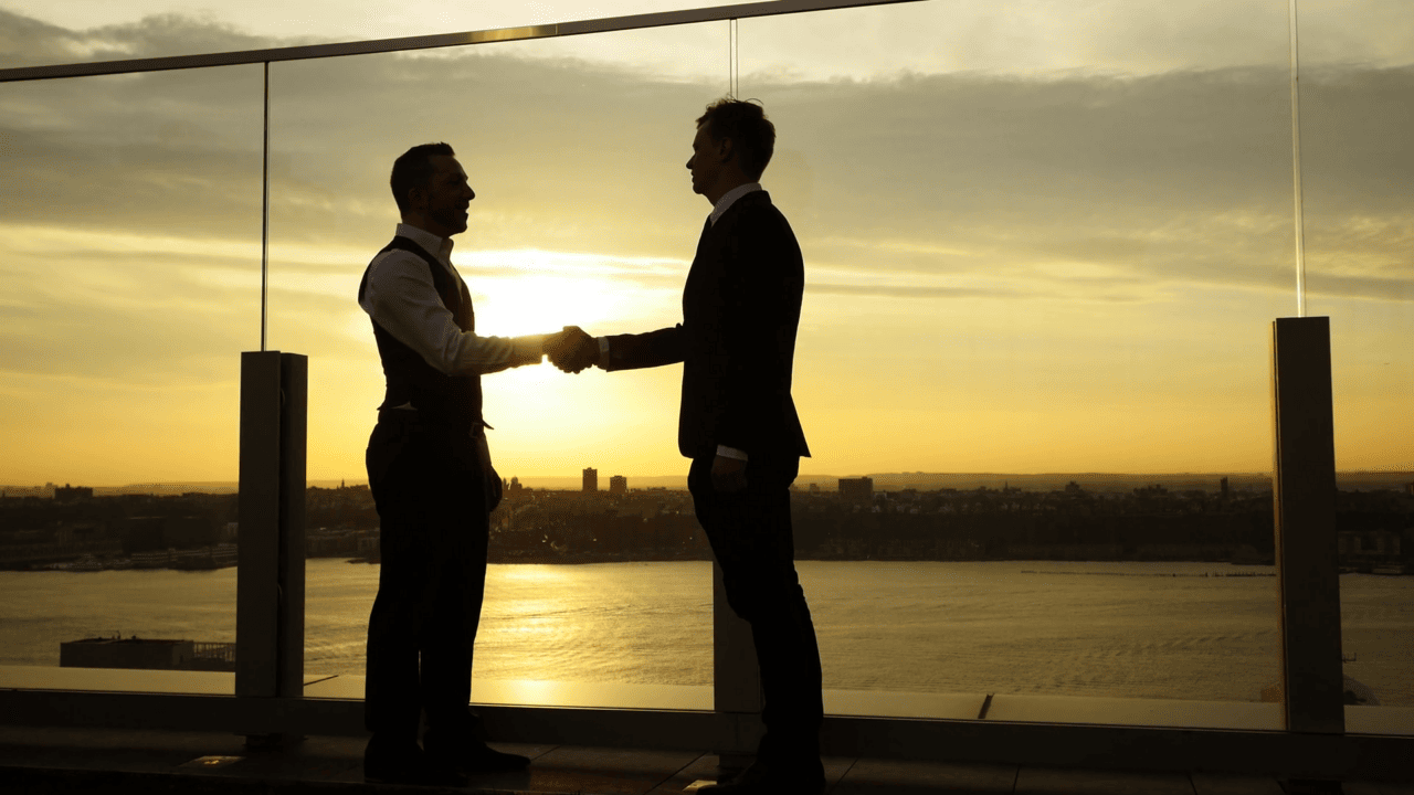 two men shaking hands in front of a sunset