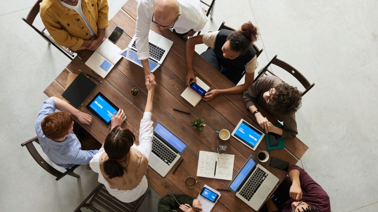 a group of people sitting around a table with laptops a group of people sitting around a table with laptops
