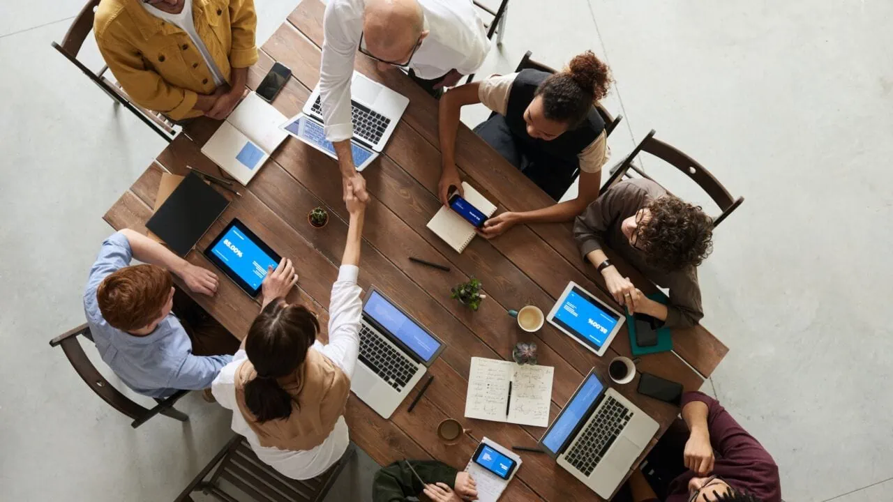 a group of people sitting around a table with laptops