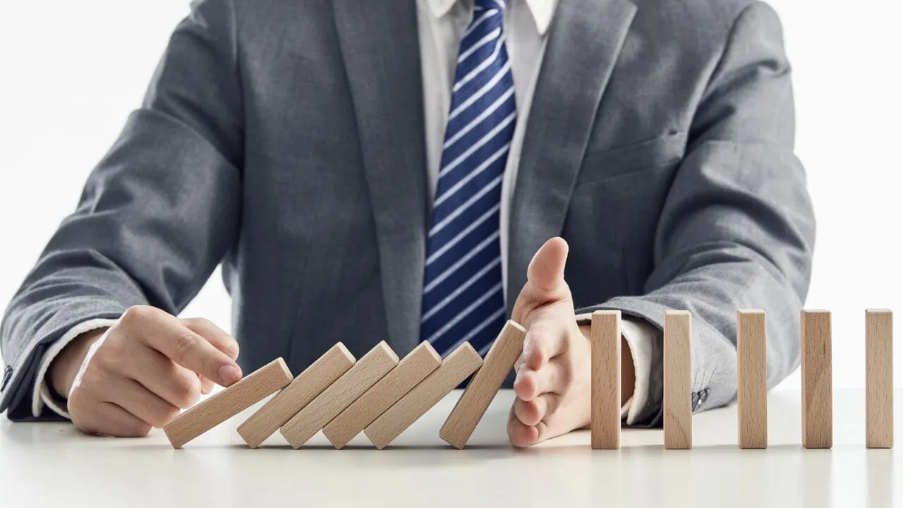 Businessman In A Suit Protecting Wooden Blocks From Falling In A Domino Effect
