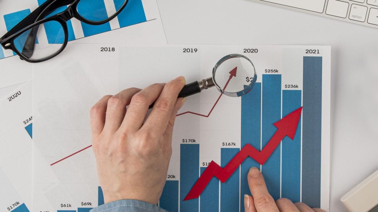 Top View Office Desk With Growth Chart Hands Holding Magnifying Glass