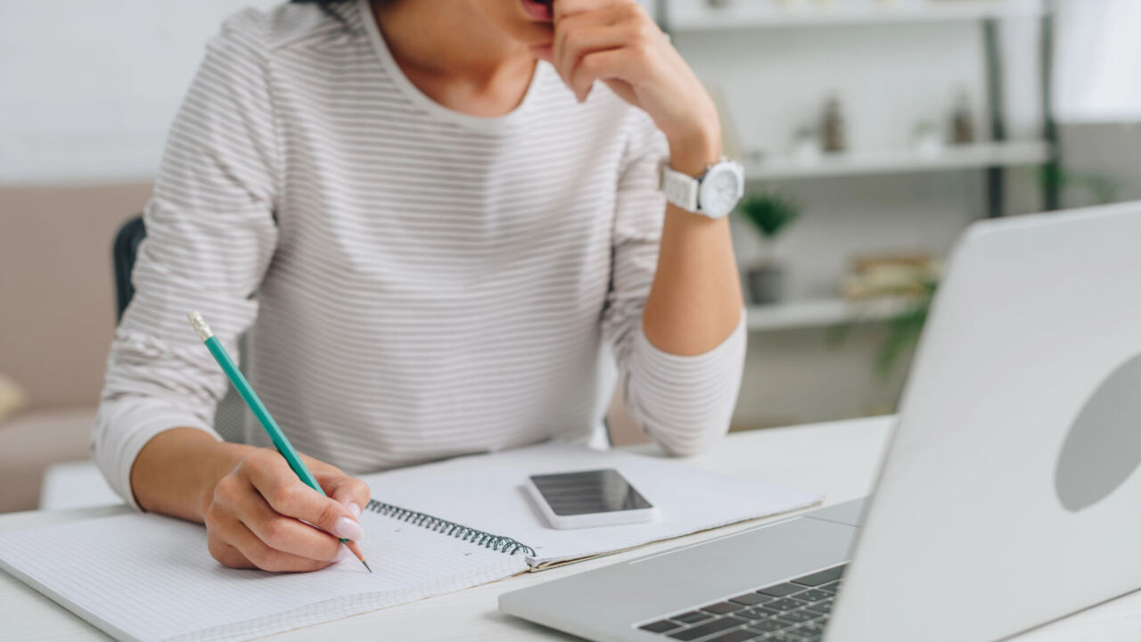 Cropped view of woman writing in notebook with pencil